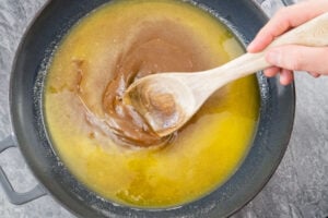 Stirring the melted butter, brown sugar and syrup together with a wooden spoon in a cast iron pan